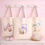 Personalised Easter tote bags with watercolour bunny and alphabet initials hanging on a white rack.