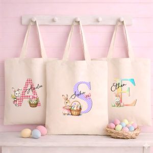 Personalised Easter tote bags with watercolour bunny and alphabet initials hanging on a white rack.
