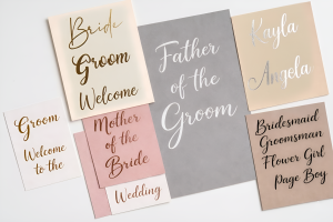 A collection of custom permanent vinyl name decals for weddings, featuring personalised names precision-cut into various coloured vinyls, including metallic gold and bright pink, displayed on a clean white background.